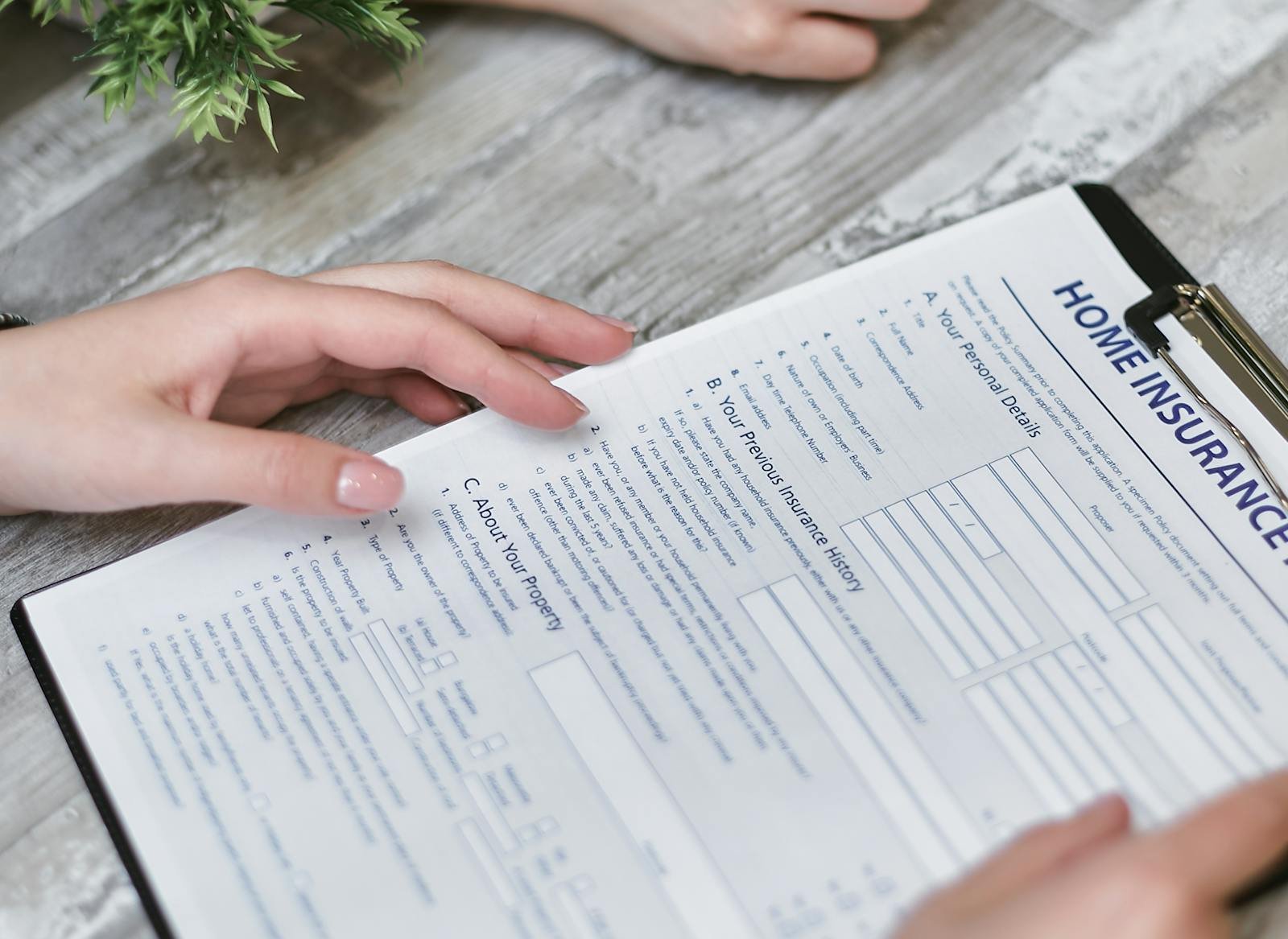 Close-up of hands holding a home insurance document indoors, showing personal details section.